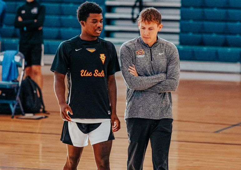 Matt Lynch stands on a basketball court with a player