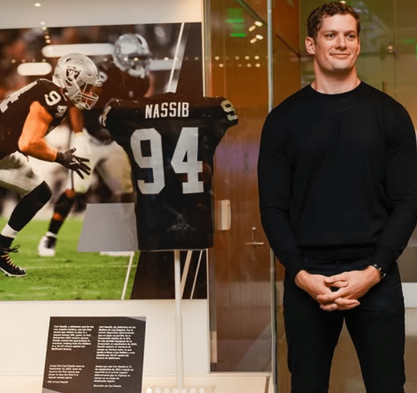 Carl Nassib, dressed in a black pullover with dark pants, stands in front of his display at the Smithsonian National Museum of American History.
